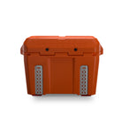 Orange‑tan Pilot Outdoors hard‑shell cooler chest, shown from a side‑front angle with lid, latch, and textured surface visible.